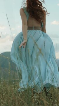 Slow motion vertical video redhead woman running through grass field back view opening arms wide dress flowing wind cinematic lifestyle freedom inspiration adventure nature