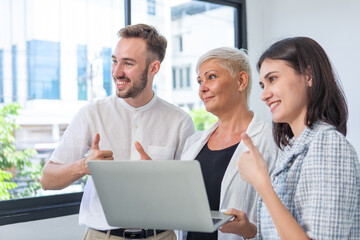 Smiling team of diverse professionals giving thumbs up while looking at laptop, symbolizing business success, team achievement, collaboration, and positive workplace culture.