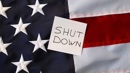 Shutdown text on note over American flag, symbol of political crisis, budget conflict and federal...