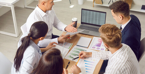 Obraz premium Dedicated business team is working together in an office, using a laptop and handling financial documents during a meeting. Colleagues collaborate on accounting tasks to ensure smooth operations.