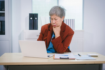 Senior Asian woman with professional office experience, focusing on reviewing financial reports and investment documents, reflecting her expertise in business, finance, and investment strategy