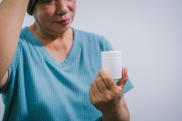 An elderly Asian woman wearing a brown-gray beanie sits quietly holding a bottle of chemotherapy...