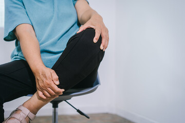 Close-up of an elderly Asian woman experiencing knee pain, reflecting common age-related conditions like osteoarthritis, gout, or inflammation, managed with physical therapy, supportive devices