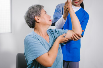 An Asian female nurse provides caring home care to an elderly woman, assisting with arm movement exercises, physical therapy,and rehabilitation to improve joint function, strength,overall well-being