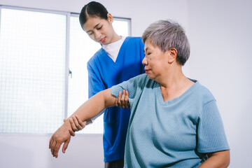 An Asian female nurse provides caring home care to an elderly woman, assisting with arm movement exercises, physical therapy,and rehabilitation to improve joint function, strength,overall well-being