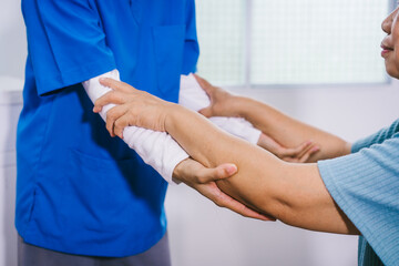 An Asian female nurse provides caring home care to an elderly woman, assisting with arm movement exercises, physical therapy,and rehabilitation to improve joint function, strength,overall well-being