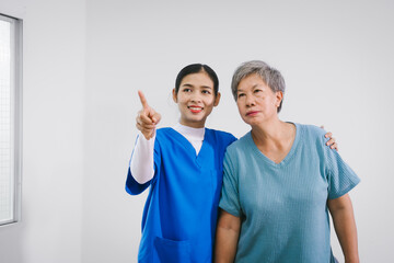 An Asian female nurse provides caring home care to an elderly woman, assisting with arm movement exercises, physical therapy,and rehabilitation to improve joint function, strength,overall well-being