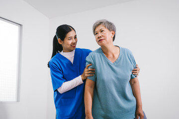 An Asian female nurse provides caring home care to an elderly woman, assisting with arm movement exercises, physical therapy,and rehabilitation to improve joint function, strength,overall well-being