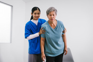 An Asian female nurse provides caring home care to an elderly woman, assisting with arm movement exercises, physical therapy,and rehabilitation to improve joint function, strength,overall well-being