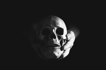 Hands holding scary evil dark grungy human skull on black background