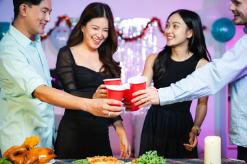 young friends raise red party cups in celebration at a fun indoor dinner party with food, laughter, and festive decorations in a colorful neon lit home