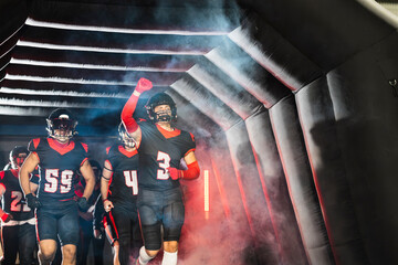 American football players emerging from a dark tunnel onto the field, celebrating with raised arms and ready for the game