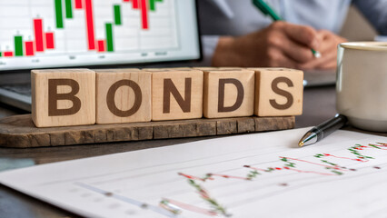 Financial bonds investment concept with wooden cubes spelling bonds, stock market chart, and analyst hands, symbolizing finance, economy, and trading strategy growth