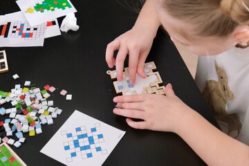 Obraz premium A girl makes a Christmas toy with her own hands from ceramic mosaic. Ceramic mosaic, DIY Christmas tree toy. Eco-friendly toy, educational activity for children. 