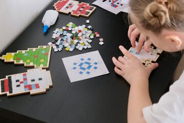 A girl makes a Christmas toy with her own hands from ceramic mosaic. Ceramic mosaic, DIY Christmas tree toy. Eco-friendly toy, educational activity for children.	