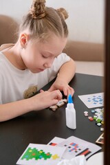 A girl makes a Christmas toy with her own hands from ceramic mosaic. Ceramic mosaic, DIY Christmas tree toy. Eco-friendly toy, educational activity for children.	