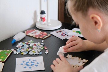 A girl makes a Christmas toy with her own hands from ceramic mosaic. Ceramic mosaic, DIY Christmas tree toy. Eco-friendly toy, educational activity for children.	