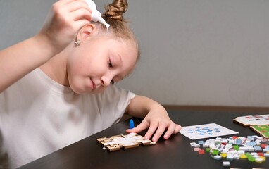 A girl makes a Christmas toy with her own hands from ceramic mosaic. Ceramic mosaic, DIY Christmas tree toy. Eco-friendly toy, educational activity for children.	