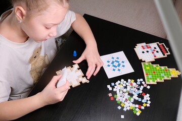 A girl makes a Christmas toy with her own hands from ceramic mosaic. Ceramic mosaic, DIY Christmas tree toy. Eco-friendly toy, educational activity for children.	