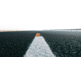Low-angle view of a straight, vanishing asphalt road with faded white and yellow lines, disappearing into a hazy horizon under a bright sky