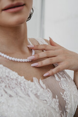 The bride in a white dress of modern design with a large neckline and a necklace around her neck placed her palm on it, demonstrating her manicure