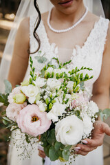 Bride in a white contemporary dress with a plunging neckline and a necklace holding a bouquet of white roses on her wedding day