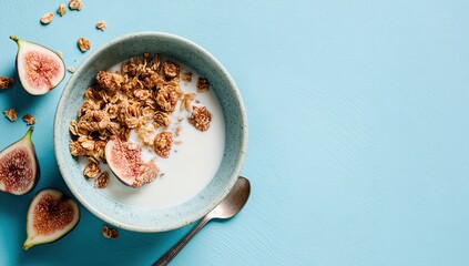 A bowl of granola with milk and fresh figs on a light blue background. Scattered oats and a spoon are also present