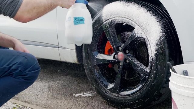 Spraying foam cleaner onto blac alloy wheels and tyres on white SYV
