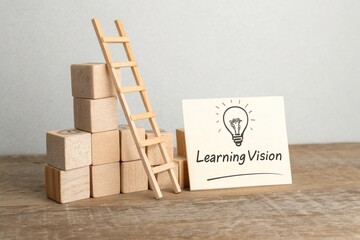 Wooden blocks stacked with a small ladder beside a sign reading 'Learning Vision' on a table