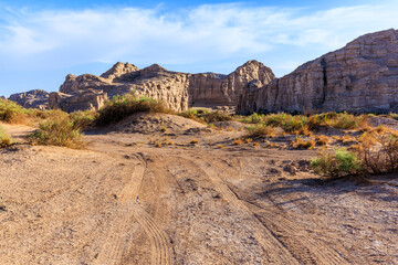 A dirt road with tire tracks through the spectacular Yardang landform mountain scenery in the desert, Xinjiang, China.