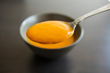 A close-up stock photo of smooth, silky pumpkin puree in a bowl on a dark background