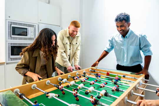 Diverse coworkers playing foosball game during office break