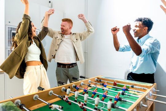 Diverse friends celebrating foosball game victory in office - Powered by Adobe