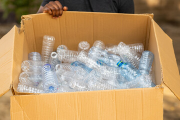 African man holding a cardboard box full of plastic bottles for recycling. Environmental awareness.