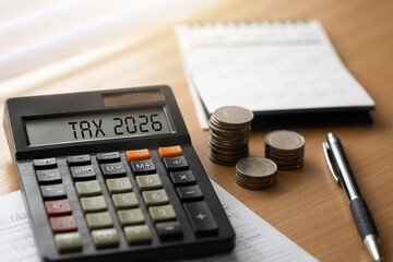 Tax planning concept with calculator showing TAX 2026, stacked coins, calendar, pen, and documents on a wooden desk. ideal for filing season tips, budgeting, business finance, deadlines, and savings.