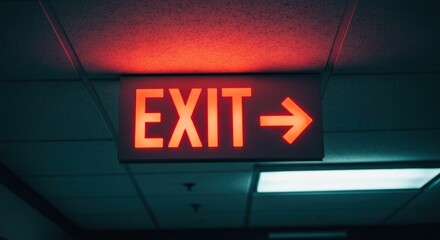 Lit red exit sign pointing right under a dim, shadowed drop ceiling