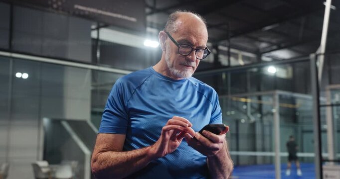 Typing, coach or elderly man in club with phone, scroll or message update during training break. Digital, sport or old person in court with mobile, tournament results or tennis tips on social media.