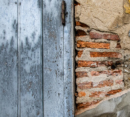 Old weathered wall with peeling plaster revealing red bricks and antique wooden door. Rustic textured background with copy space for vintage or design use.