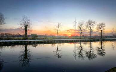 A tranquil sunset casts vibrant colors brilliantly over the still waters, framed beautifully by silhouetted trees