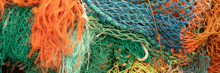 Panorama of pile of colourful fishing nets on a quayside for use as a background texture