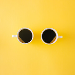 Creative concept made with two white cup of morrning coffee on a yellow backround with copy space.Minimal flat lay