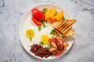A delicious breakfast with sunny-side up eggs, crispy bacon, beans, and fresh veggies