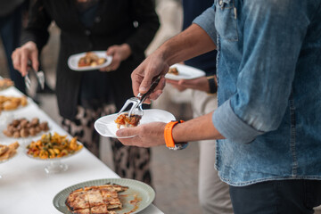 Guests at an elegant private event enjoy a gourmet buffet selection of delicious catered food items displayed on a long table in a bright airy venue with people serving themselves from various dishes