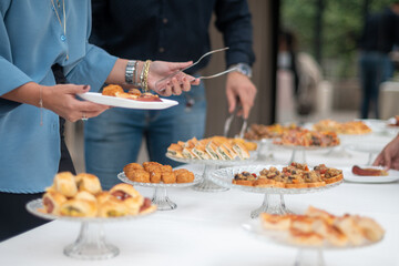 People serving themselves delicious appetizers and finger foods from a buffet table at an outdoor gathering or event showcasing a variety of tasty treats laid out on elegant display stands for guests