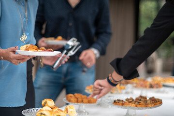 People gathering around a buffet table selecting small appetizers and finger foods during an...