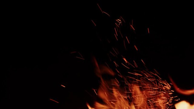 Small fire sparks and flames glowing on a black background at night, with visible fiery tongues creating a dramatic burning effect