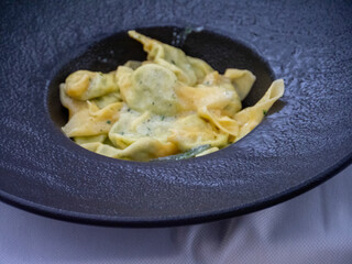 Delicious overhead shot of vibrant vegan tortelli stuffed pasta with a creamy green sauce in a rustic dark bowl on a light textured tablecloth