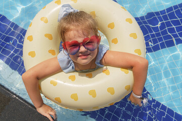 Portrait of a little girl floating with rubber ring in outdoor swimming pool 