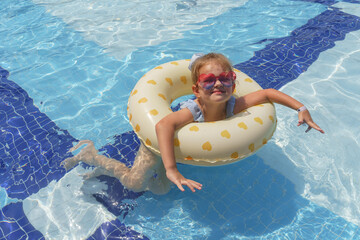 A little blond girl swimming with inflatable ring in swimming pool 