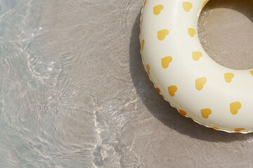 top-down view of a white inflatable ring adorned with yellow hearts resting on wet sand at the edge of clear, rippling water